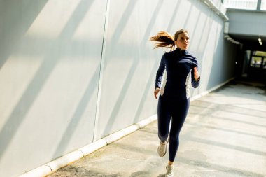 Kendini adamış bir koşucu parlak, güneşli bir patika boyunca yarışır. Şehrin hareketli kalbine çağdaş binalarla çevrili uzun gölgeler bırakır..