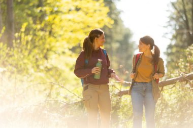 İki arkadaş, altın yapraklar ve yüksek ağaçlarla çevrili güneşli yürüyüş yolunda kahkahalarını paylaşıyor. Doğada değerli anılar yaratıyorlar..