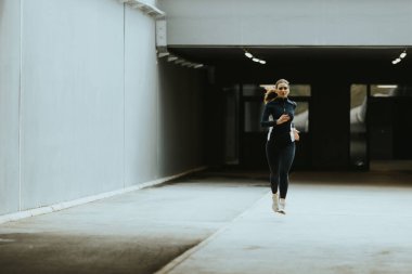 Kararlı bir koşucu, sakin bir sabah atmosferinde spor salonuna ve temposunun ritmine odaklanarak boş bir şehir koridorunda yol alır..