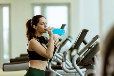 Kadınlar sabah saatlerinde spor malzemeleriyle dolu açık, havadar bir spor salonunda dinlenirken ferahlatıcı bir içkiden hoşlanırlar..