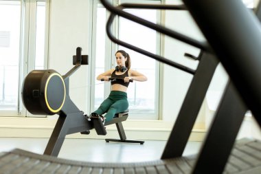Adanmış bir sporcu kürek egzersizi yapar, gösterişli ve iyi aydınlatılmış bir spor salonu atmosferinde bağlılığını ve gücünü gösterir..