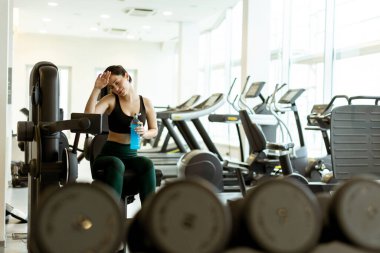 Parlak bir fitness stüdyosunda, bir kadın susuzluğunu gidermek, azmi somutlaştırmak ve fitness yolculuğuna odaklanmak için duraklarken bacak uzantılarını gerçekleştirir..