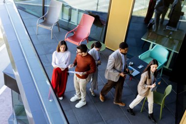 Beş profesyonelden oluşan çeşitli bir grup, lüks bir terasta dijital tabletleri incelerken canlı tartışmalara giriyorlar. Güneş ışığı kıyafetlerine neşe saçar..