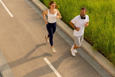 İki hevesli koşucu, yemyeşil yemyeşil bir yolda sakin bir sabah koşarken gülüşlerini paylaşıyor..