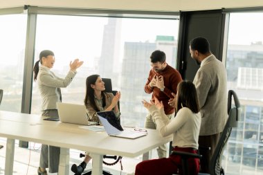 Bir grup profesyonel, geniş pencereleri ve doğal ışığı olan çağdaş bir ofiste proje planlarını aktif olarak tartışıyor. Müdahaleleri takım çalışması ve yenilik sürecini yansıtıyor.