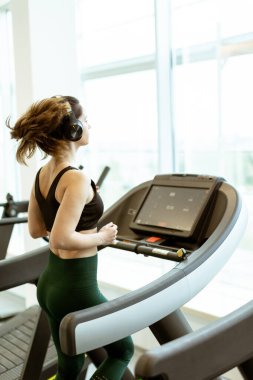 Adanmış bir koşucu, modern bir spor salonunda doğal ışıkla çevrili bir koşu bandında spor yapar..