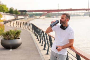Parlak bir günde, nehir kenarındaki patika boyunca uzanan korkuluklara yaslanırken koşucunun su içmesi biraz zaman alır..