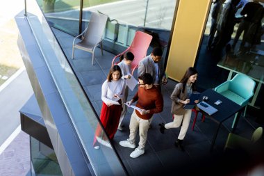 Beş profesyonelden oluşan çeşitli bir grup, lüks bir terasta dijital tabletleri incelerken canlı tartışmalara giriyorlar. Güneş ışığı kıyafetlerine neşe saçar..