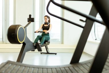 Adanmış bir sporcu kürek egzersizi yapar, gösterişli ve iyi aydınlatılmış bir spor salonu atmosferinde bağlılığını ve gücünü gösterir..