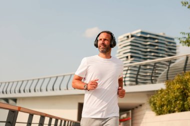 Bir adam modern bir yürüyüş yolu boyunca koşar, sabah güneşinin sıcaklığında güneşlenir ve en sevdiği melodilere daldırılır..