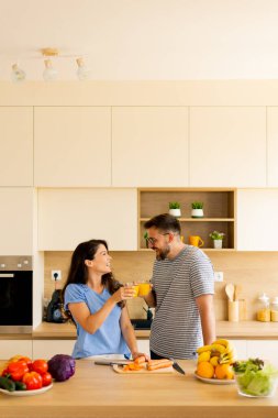 Taze meyve ve sebzelerle dolu parlak bir mutfak. Mutlu bir anı paylaşan bir çift olarak, kadehlerini yemek hazırlıkları sırasında kaldırıyorlar..