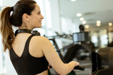 Kendini işine adamış genç bir kadın, hareketli ve modern bir spor salonunda dikkatle kürek çekmeye çalışıyor..