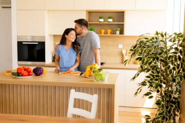 Parlak, çağdaş bir mutfakta, bir çift, taze ürünlerle çevrili lezzetli bir yemek hazırlarken keyifli bir anı paylaşıyor..