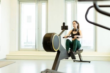 Adanmış bir sporcu kürek egzersizi yapar, gösterişli ve iyi aydınlatılmış bir spor salonu atmosferinde bağlılığını ve gücünü gösterir..