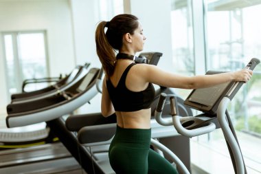 Kararlı bir kadın eliptik bir makine üzerinde egzersiz yapıyor, parlak ve modern bir spor salonunda sabah enerjisini kullanıyor..