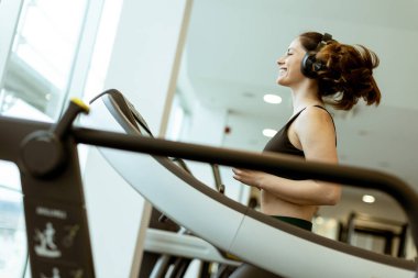 Neşeli bir atlet koşu bandında koşuyor, müziğe dalmış, gündüz saatlerinde parlak bir spor salonunda, neşeyle zindeliği kucaklıyor..