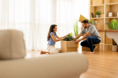 Bir çift, güneşli oturma odalarında, yeni başlangıçların sıcaklığı ve beklentisiyle çevrili kutuları neşeyle açıyor..