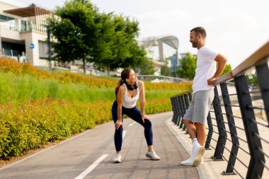 İki sporcu, açık mavi gökyüzünün altında yemyeşil bir yeşil ile bezenmiş canlı bir parkta çalışmaları sırasında keyifli bir anı paylaşıyor..