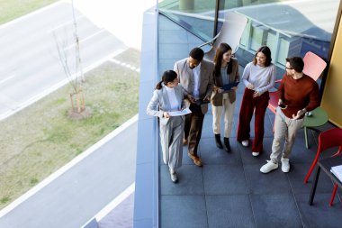 Beş profesyonelden oluşan çeşitli bir grup, lüks bir terasta dijital tabletleri incelerken canlı tartışmalara giriyorlar. Güneş ışığı kıyafetlerine neşe saçar..