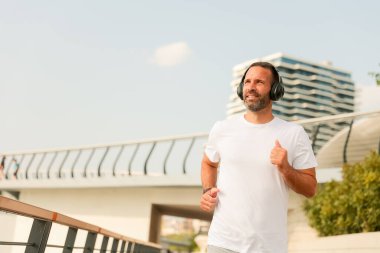 Bir adam modern bir yolda koşuyor, kulaklık takıyor ve neşeli bir ifade takıyor. Arkaplanda şık bir mimari ve parlak bir gökyüzü, enerjik bir sabah atmosferi yaratıyor..