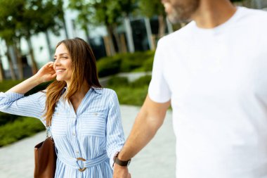 İki arkadaş güneşli bir günün sıcaklığını kucaklıyor, yemyeşil ve kahkahalarla dolu bir şehir parkında el ele yürüyor..