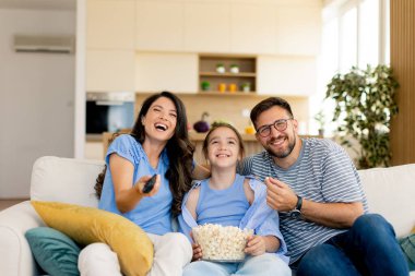 Üç aile üyesi evde film izlerken gülümseme ve kahkaha paylaşıyor. Patlamış mısır servis edilir, ve oturma odası sıcak ışıkla yıkanır, sıcak bir atmosfer yaratır..