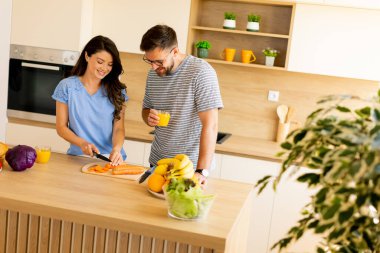 Parlak ve şık bir mutfakta, bir çift kahkahalarını paylaşırken taze sebze hazırlar..