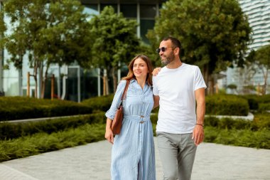 Genç bir çift, yeşillik ve çağdaş mimarinin ortasında gülümseyerek ve arkadaşlıktan zevk alarak rahat bir yürüyüş yapar..