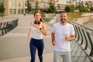 İki arkadaş nehir boyunca serinletici bir koşunun keyfini çıkarıyorlar, gülüşmeler ve şehirde aydınlık bir sabahın enerjisini paylaşıyorlar..