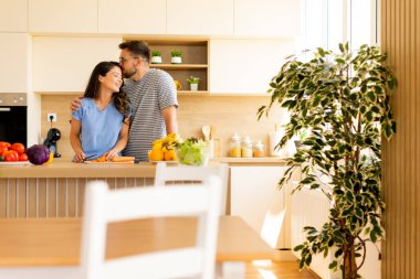 Güneşli bir mutfakta, bir çift taze sebzelerle çevrili bir yemek hazırlarken neşeli bir anı paylaşır ve sevgi ve birliktelik dolu bir atmosferi olur..