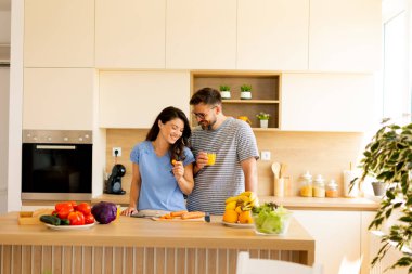 Neşeli anlar paylaşılırken bir çift taze sebze hazırlıyor ve gün ışığında yıkanan şık bir mutfakta içeceklerden zevk alıyor, yemek pişirmek için canlı ve sıcak bir atmosfer yaratıyor..