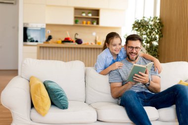 Bir baba ve kızı keyifli bir hikaye anlatma seansına dalmış, öğleden sonra saatlerinde parlak, davetkar oturma odalarında rahat bir kanepede gülüşlerini ve kahkahalarını paylaşıyorlar..