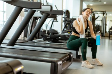 Spor kıyafetleri içinde, bir kadın spor salonunda mola verir, mavi bir içki yudumlar ve sıkı bir egzersizin ardından sakin bir anın tadını çıkarır..