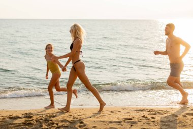 İki kadın ve bir kız gün batımında neşeyle koşar, kahkahaları hafif dalgalarla taşınır. Altın renkler mükemmel bir aile birlikteliği anını yansıtıyor..