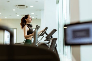 İyi ışıklandırılmış bir spor salonundaki eliptik bir makineye odaklanmış birey sabah güneşinin tadını çıkarırken büyük pencerelerden içeri dökülüyor..