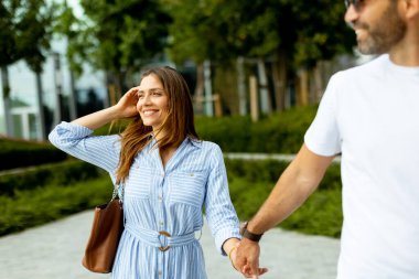 İki arkadaş güneşli bir günün sıcaklığını kucaklıyor, yemyeşil ve kahkahalarla dolu bir şehir parkında el ele yürüyor..