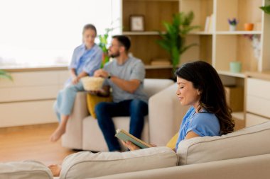 Sıcak ve davetkar bir oturma odasında, bir arkadaş kitap okurken diğerleri rahatlıyor, atıştırmalıkları ve kahkahaları paylaşıyor, keyifli bir öğleden sonrası için mükemmel sıcak bir ortam yaratıyor..