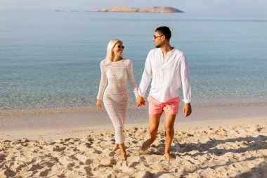 İki aşık el ele yürür el ele, el ele, el ele, narin dalgalar ayaklarına vurur ve gökyüzünü boyayan sakin bir günbatımı, onların anı için mükemmel bir zemin yaratır..