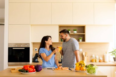Taze meyve ve sebzelerle dolu parlak bir mutfak. Mutlu bir anı paylaşan bir çift olarak, kadehlerini yemek hazırlıkları sırasında kaldırıyorlar..