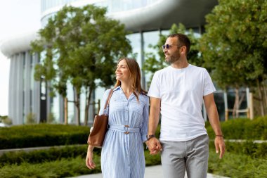 Berrak bir gökyüzü altında, yemyeşil ve çağdaş binaların arasında gülümseyen, el ele tutuşan iki insan..