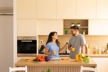 İki arkadaş, şık bir mutfakta taze malzemeler hazırlarken ve birlikte geçirdikleri zamanın tadını çıkarırken keyifli bir anın tadını çıkarıyorlar. Parlak meyve ve sebzeler tezgahı süslüyor..