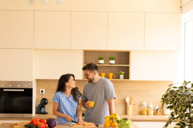 Geniş, çağdaş bir mutfakta iki arkadaş sebze doğrayıp içeceklerin tadını çıkarırken keyifli bir anı paylaşıyorlar. Taze malzemeler serildi, neşeli atmosferi güçlendirdi..