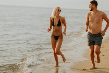 Bir çift kıyı şeridi boyunca koşuyor, gülüyor ve sakin sahil atmosferinin tadını çıkarıyor. Güneş arka planda batarken, parlak bir gökyüzü yaratıyor..