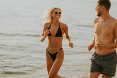 Sahilde güneşli bir günde gülerek ve neşe dolu bir anı paylaşarak koşan iki arkadaş havaya su sıçratır..