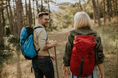 Bir adam ve bir kadın yemyeşil bir orman yolunda yürüyor, sohbet ediyor ve gülümsüyor. Güneş ağaçların arasından süzülerek, açık hava maceraları için sıcak ve davetkar bir atmosfer yaratır..