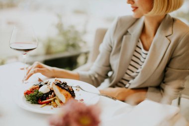 Şık kıyafetli bir kadın, öğlenleri sıcak bir restoranda canlı sebzeler ve bir bardak kırmızı şarapla gurme yemeğinden hoşlanır..