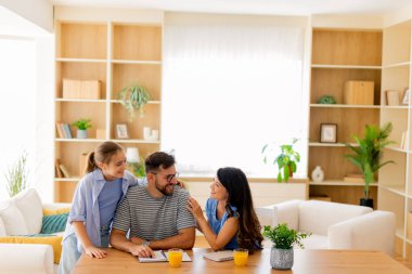 Bir babanın kızlarıyla neşeli bir şekilde, bitkilerle ve gülümsemelerle çevrili, güneşli bir yaşam alanında etkileşime girdiği neşeli bir an başlıyor..