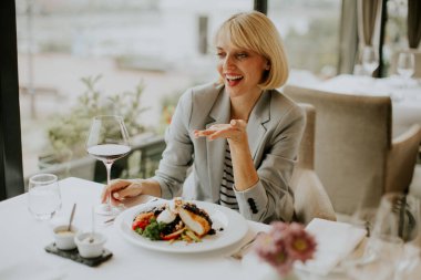Modern bir restoranın masasında şık bir ceket giymiş bir kadın oturuyor..