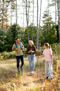 Üç aile üyesi, ağaçlarla çevrili güneşli bir yolda yürürken neşeli bir ormanı keşfeder, kahkahalar ve hikayeler paylaşırlar..