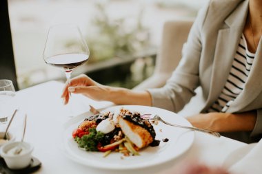 Diners relax at a chic restaurant, savoring a beautifully plated dish of chicken with a rich sauce and a glass of red wine during an elegant evening meal.